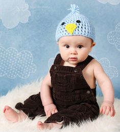 a baby wearing a knitted bird hat sitting on top of a fluffy white blanket