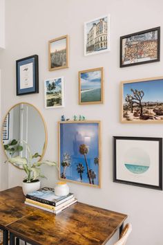 a wooden table topped with lots of pictures and framed art on the wall above it