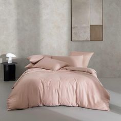 a bed with pink sheets and pillows in a room next to a painting on the wall