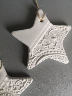 two white ceramic ornaments hanging from a string on a gray wall, one with a star ornament