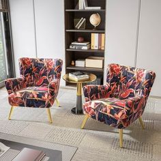 two colorful chairs sitting in front of a book shelf next to a table with books on it