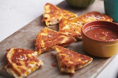 several pieces of pizza on a cutting board with dipping sauce