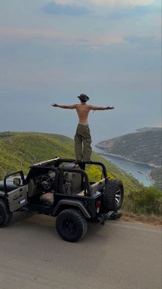 a man standing on top of a jeep with his arms wide open in front of him