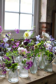 Glass bud vases filled with seasonal purple flowers sit next to a window Home Table Decorations, Purple Wedding Tables, Bud Vases Wedding, Bud Vases Arrangements, Round Wedding Tables, Wedding Floral Arrangements, Bud Vases Flowers, Glass Bud Vases, Neutral Wedding Flowers