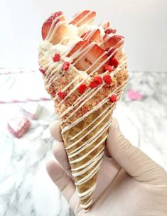 a hand holding an ice cream cone with strawberries and whip cream drizzled on top