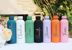 six personalized water bottles lined up on a table with flowers in the foreground