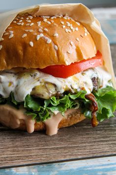 a burger with lettuce, tomato and cheese on it sitting on a wooden table