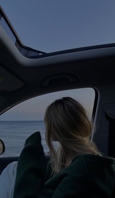 a woman sitting in the passenger seat of a car looking out at the ocean