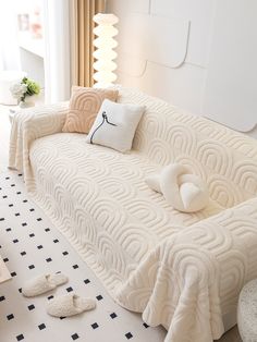 a white couch with pillows on top of it and two slippers laying on the floor