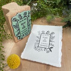 a wooden block with an embroidered cloth on it next to a flower pot and plant