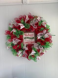 a red and green christmas wreath hanging on the side of a white wall next to a sign