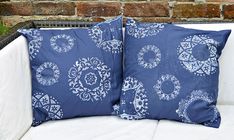 two blue and white pillows sitting on top of a couch next to a brick wall