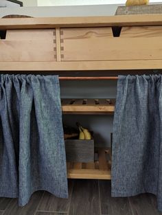 the bottom half of a bunk bed with blue curtains and two bananas on it's shelf