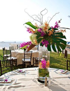 a vase filled with flowers sitting on top of a table next to the ocean and grass