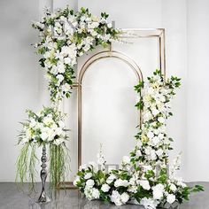 white flowers and greenery are arranged in front of an ornate mirror on a table