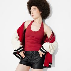 a woman with an afro standing in front of a white wall wearing black leather shorts and a red top