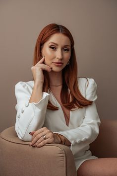 a woman sitting on top of a brown chair with her hand under her chin and looking at the camera