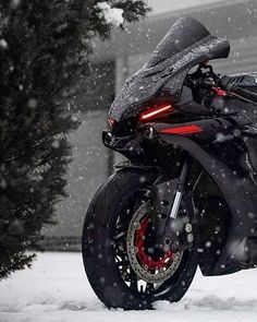 a black motorcycle parked in the snow near a tree and building with lights on it