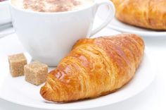 there is a croissant on the plate next to a cup of coffee and sugar cubes