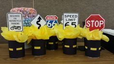 there are many road signs on the table with yellow tissue paper flowers in black vases