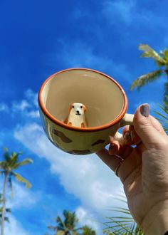 a hand holding a coffee cup with a dog in the middle and palm trees behind it