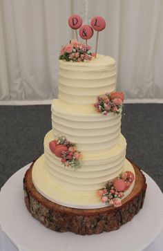 a three tiered wedding cake with pink flowers on the top and initials on the side