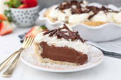 a slice of chocolate cream pie on a plate with a fork and bowl of strawberries in the background