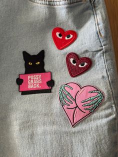 three different patches on the back of a person's jean pants, one with a black cat and two red hearts