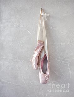 two ballet shoes hanging on a wall with one being tied to the side by a string