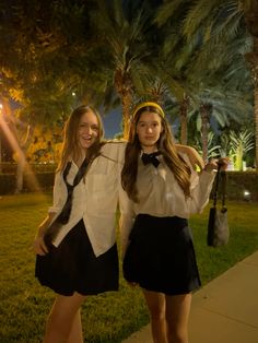 two girls dressed in school uniforms posing for the camera at night with palm trees behind them