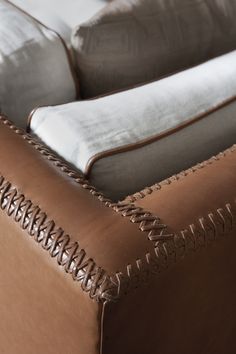 a brown leather couch sitting on top of a wooden floor next to a white pillow