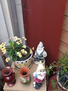 pots with flowers and gnome figurines are on the ground next to a red door