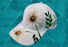 a white baseball cap with flowers painted on it's front and side panels, sitting against a blue background