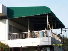 two men are standing on the balcony of a building with a green awning over it