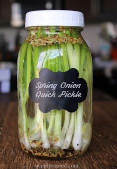 a jar filled with green onions sitting on top of a wooden table