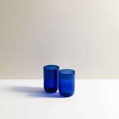 two blue glass cups sitting on top of a white table next to eachother