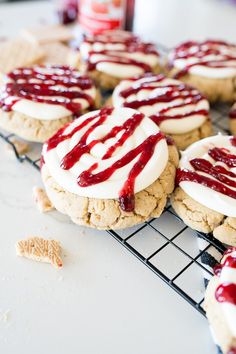 cookies with white frosting and red sauce on top are cooling on a wire rack