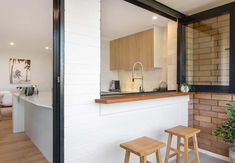 an open kitchen and living room area with brick walls, wood flooring and stools