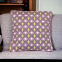 a purple and yellow pillow sitting on top of a gray couch next to a book shelf