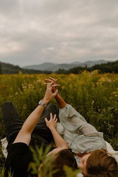 two people laying in the grass touching hands