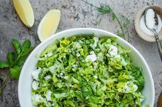 a white bowl filled with lettuce next to sliced lemons and garlic on top of a table