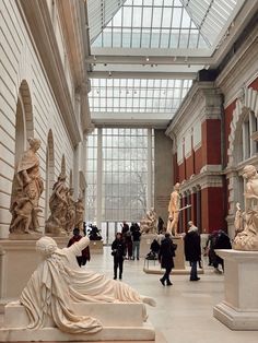 many people are looking at statues in a museum with glass walls and windows on the ceiling