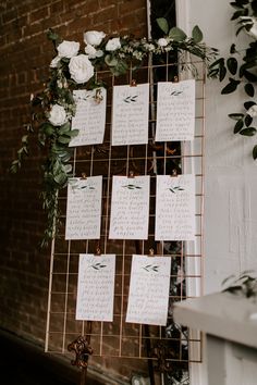 wedding seating chart with flowers and greenery hanging on the side of a brick wall