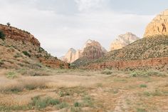 an empty field with mountains in the background and grass growing on the ground near by