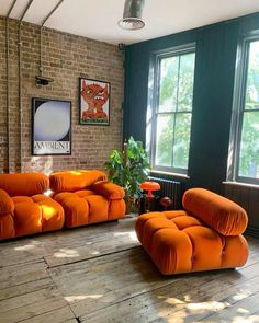 an orange couch and chair sitting in front of two windows next to a brick wall