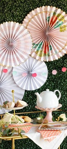 there are many paper fans hanging on the wall behind a table with plates and cups