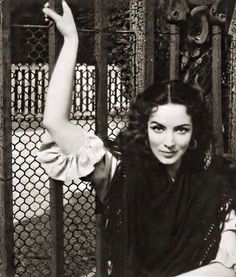 an old photo of a woman leaning on a fence with her arm up in the air