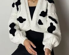 a woman sitting on a stool wearing a cow print cardigan sweater and black pants