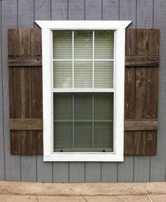 a window with wooden shutters on the side of a gray wall and concrete floor