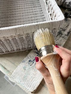 a woman holding a paint brush in her hand next to some wicker basketes